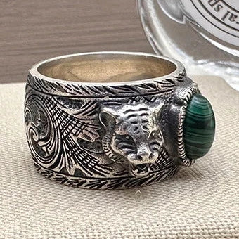 Silver ring with tiger design and green stone on a beige surface