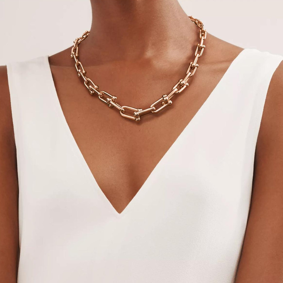 Rose gold chain necklace worn by a model in a white dress on a light background