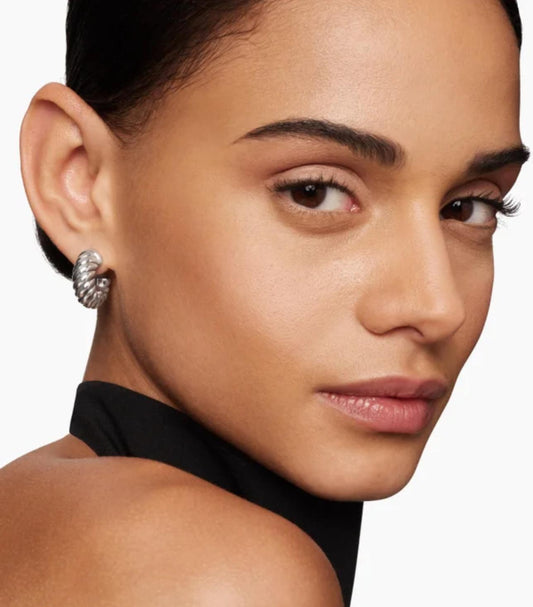 Close-up of a woman's face with a focus on her earring against a neutral background