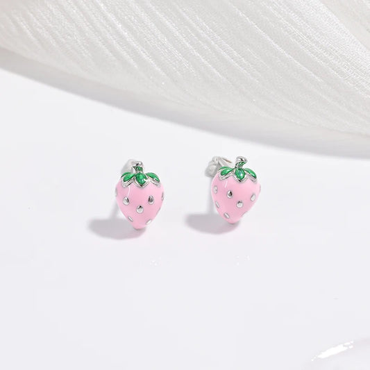 A collection of children's jewelry featuring studs in the shapes of cherries, strawberries, and festive trees, with a white and green color scheme.