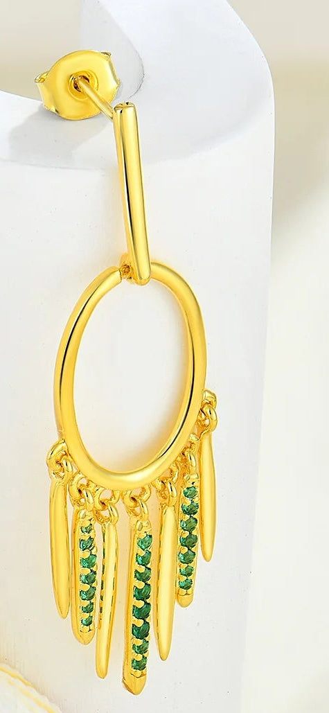 Gold earrings with green gemstones on a white shell background