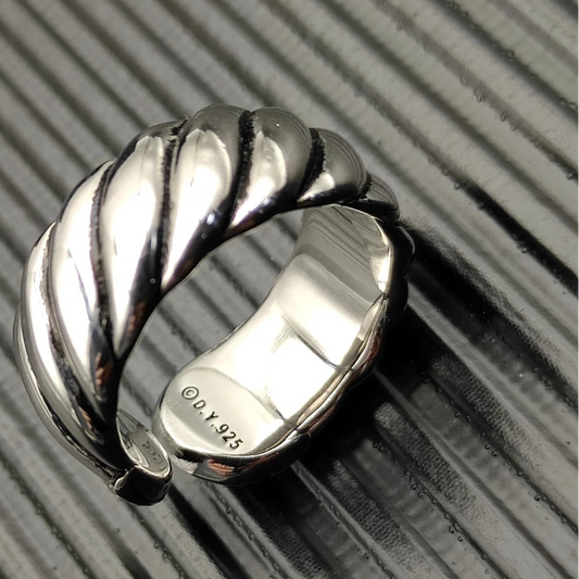 A silver spiral ring with a textured band and a shiny finish, displayed on a ribbed surface.