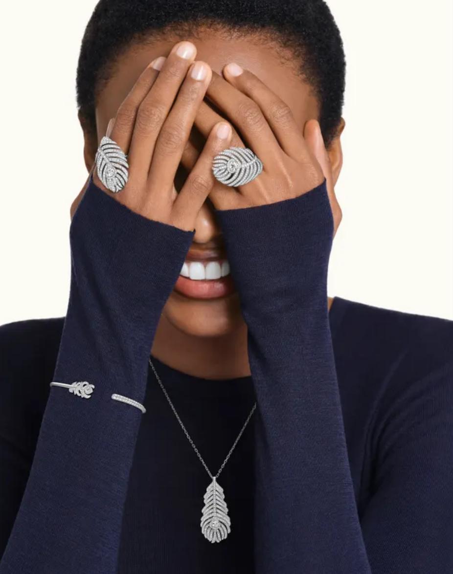 Person wearing silver feather-shaped rings and a necklace with a white background