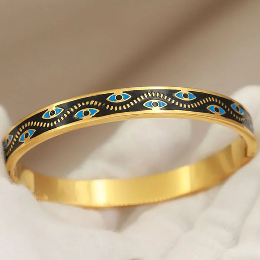 Two bangles with gold-color plating, one featuring a black background with blue eyes and floral accents, and the other with a white background showing a similar design.