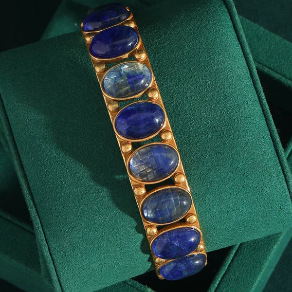 A wrap-style bracelet with a blue opal centerpiece and vintage gold-tone settings, displayed on a green cushion.