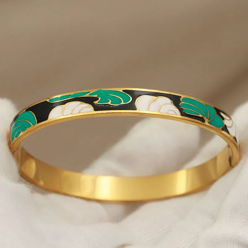 Gold bracelet with green and black floral patterns on a beige background