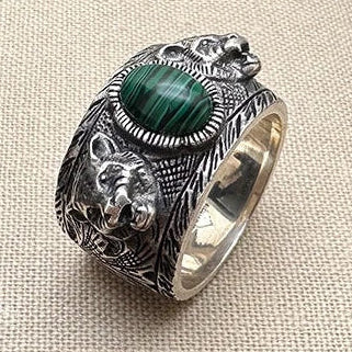 Silver ring with green stone and bear design on a beige fabric background