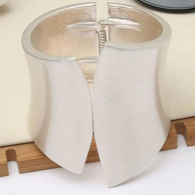 Silver cuff bracelet on a wooden stand with a white background