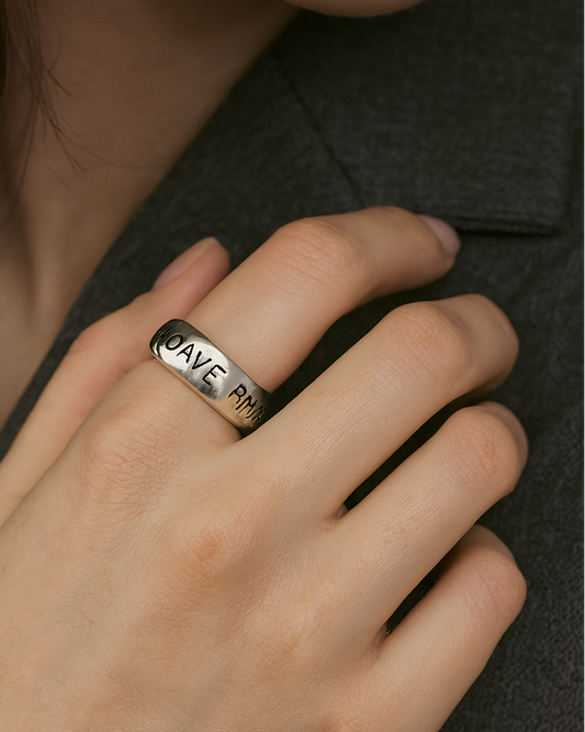 Silver ring with engraved text on a person's finger against a dark background