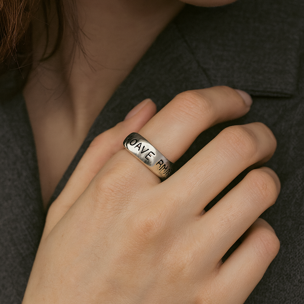Silver ring with engraved text on a person's finger against a dark background