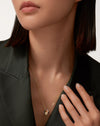 A sophisticated woman in a dark tailored blazer modeling the Harmonie Trio 18K tri-color gold interlocking pendant necklace, perfectly draped on a 24-inch PVD gold chain.