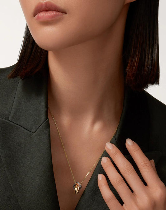 A sophisticated woman in a dark tailored blazer modeling the Harmonie Trio 18K tri-color gold interlocking pendant necklace, perfectly draped on a 24-inch PVD gold chain.