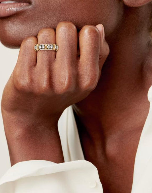 A close-up shot of a model wearing the Aurelia XVI two-tone solid 925 silver and 18K gold ring, featuring 1.14ct round brilliant moissanite stones and interlaced cross-stitch X motifs.