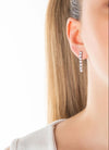 Close-up of a person wearing a silver 'BAMBERG' earring on a white background