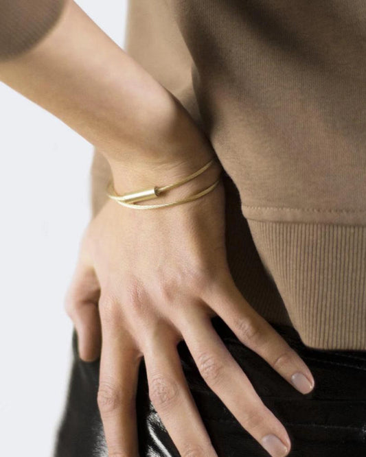 Close-up of a person wearing a gold bracelet on a plain background