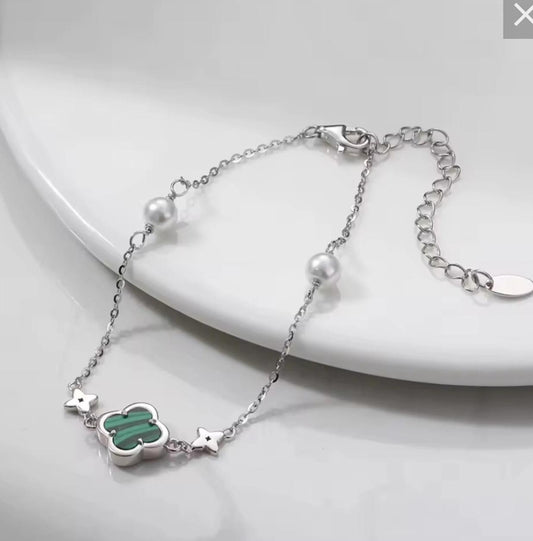 Silver bracelet with green clover charm on a white plate