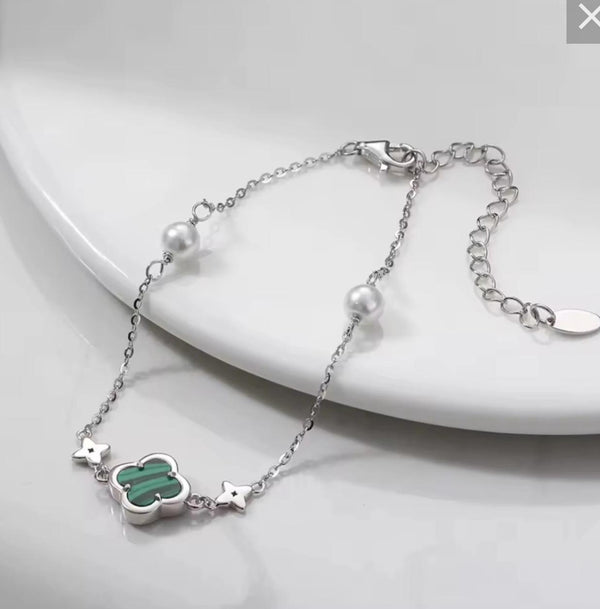 Silver bracelet with green clover charm on a white plate