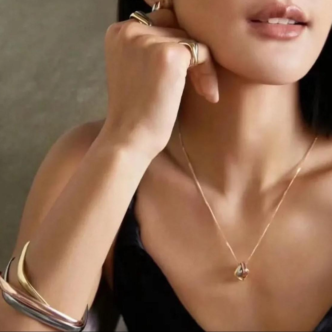 Woman wearing gold jewelry including a necklace, bracelet, and ring.