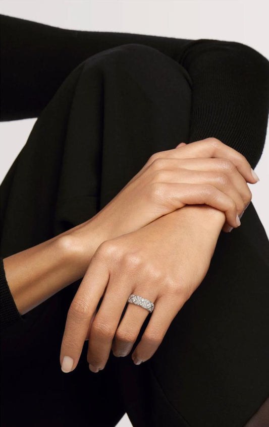 A sophisticated woman in a black elegant dress resting her hands, modeling the Matelassé 8mm wide quilted pavé moissanite ring in solid 925 silver.