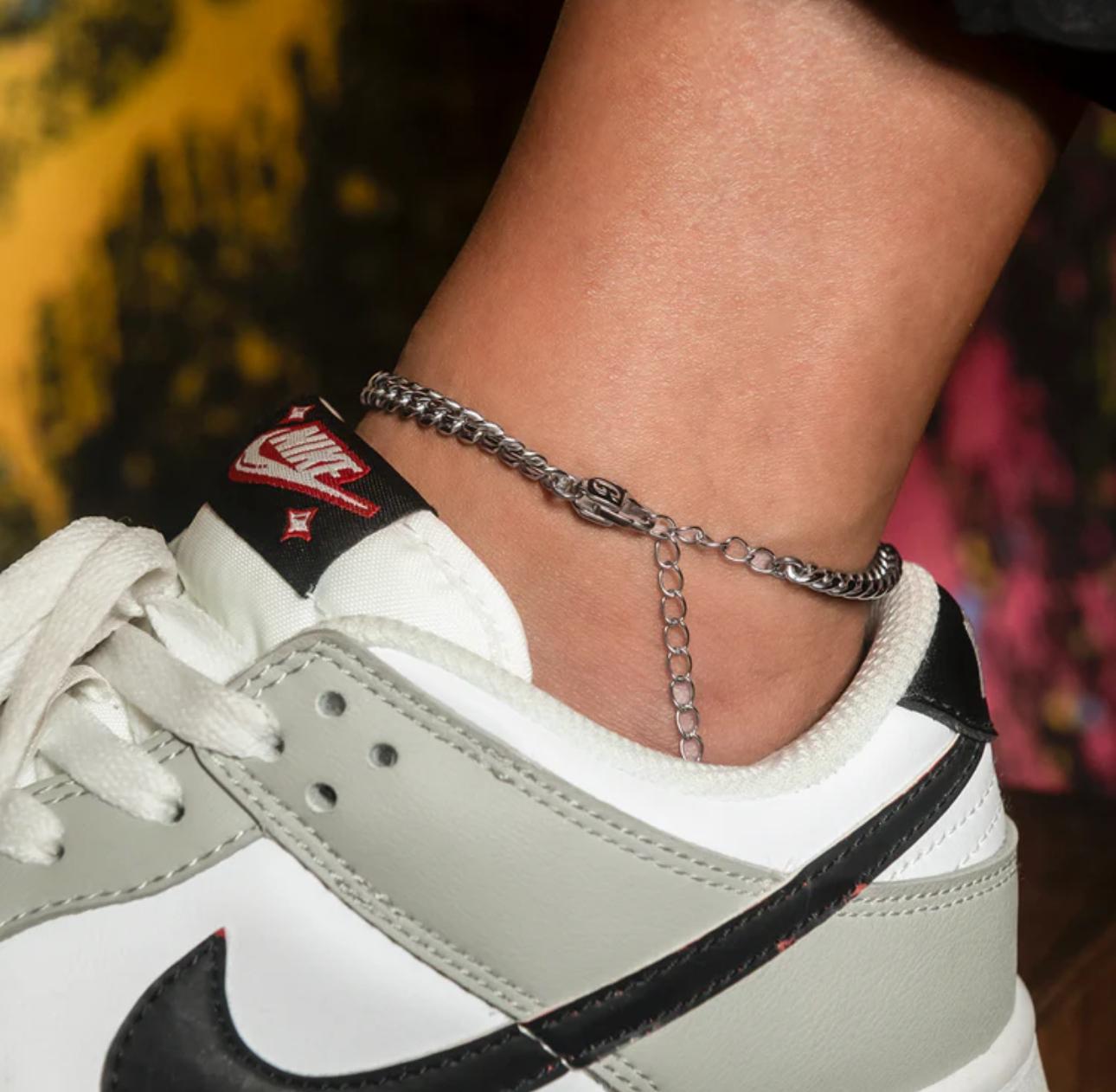 Close-up of a person wearing a silver Cuban Link Anklet with a blurred background