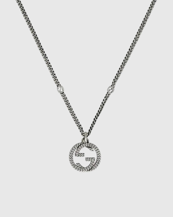 Close-up detail of the sculpted interlocking monogram charm with a twisted rope motif and antiqued oxidized finish.