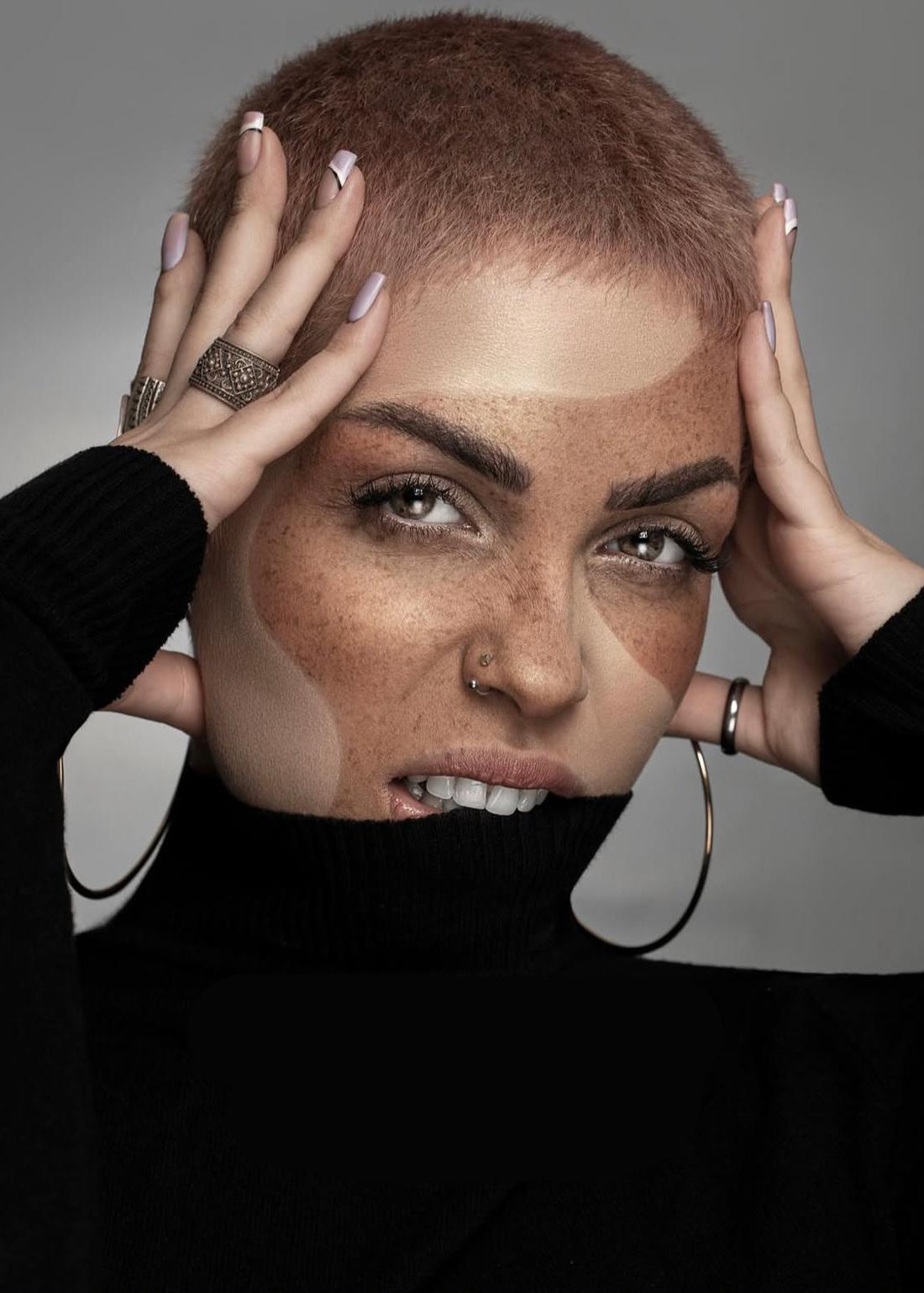 Model with shaved head holding hair, wearing a black outfit, with 'DAPPLE' branding.