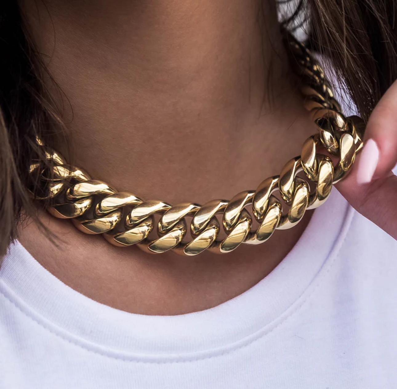Close-up of a person wearing a gold cuban link necklace with a blurred background