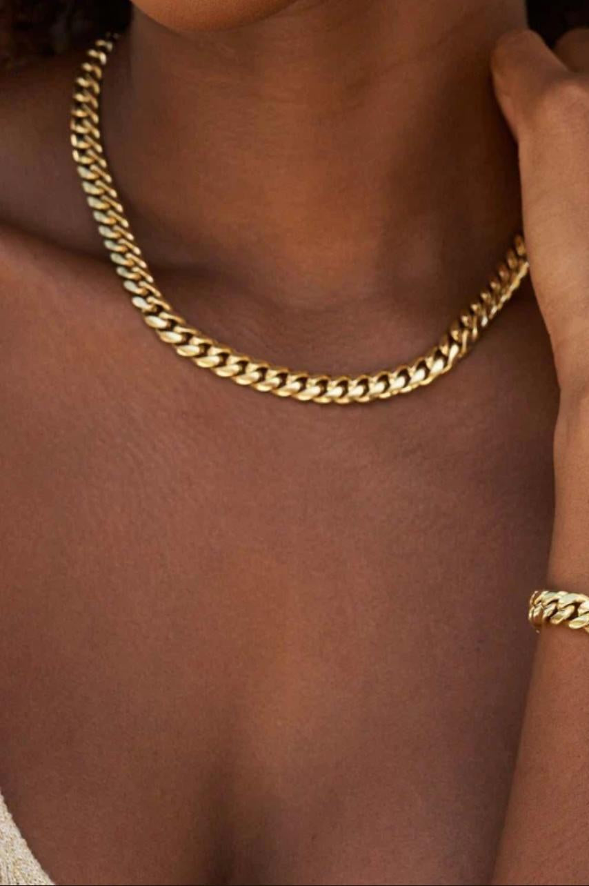 Close-up of a person wearing a gold cuban link necklace and bracelet with a blurred background
