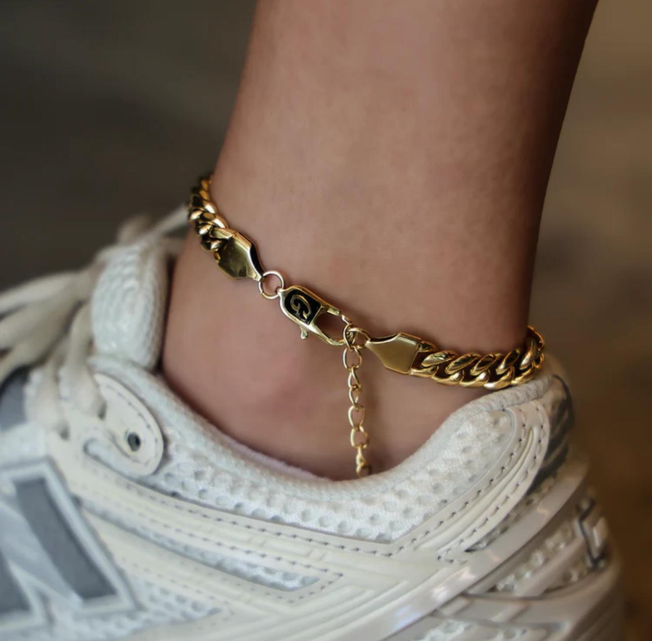Close-up of a person wearing a gold Cuban Link Anklet with a blurred background