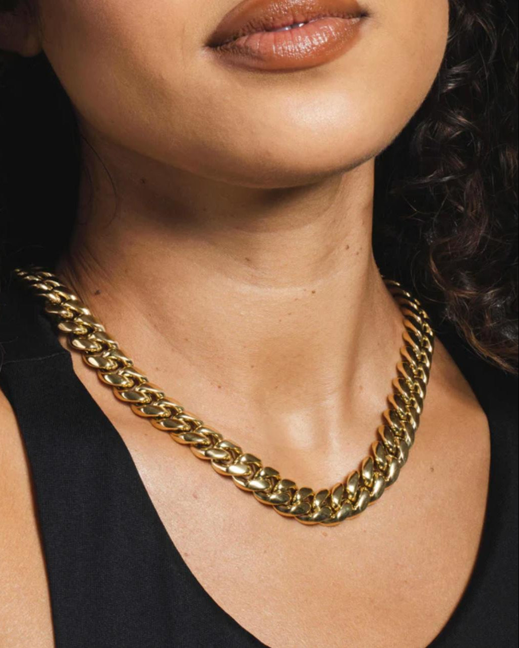 Close-up of a person wearing a gold cuban link necklace with a blurred background