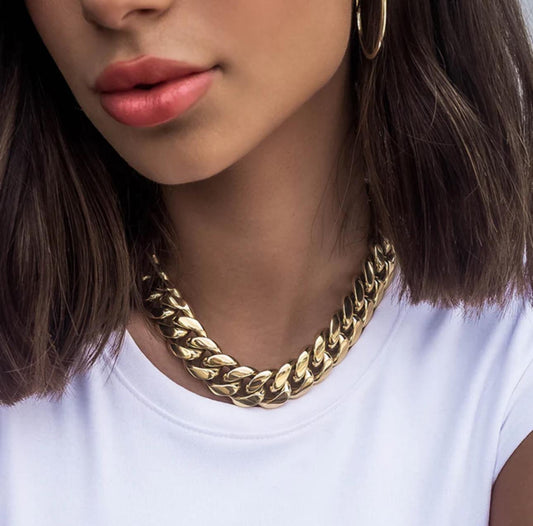Close-up of a person wearing a gold cuban link necklace with a blurred background