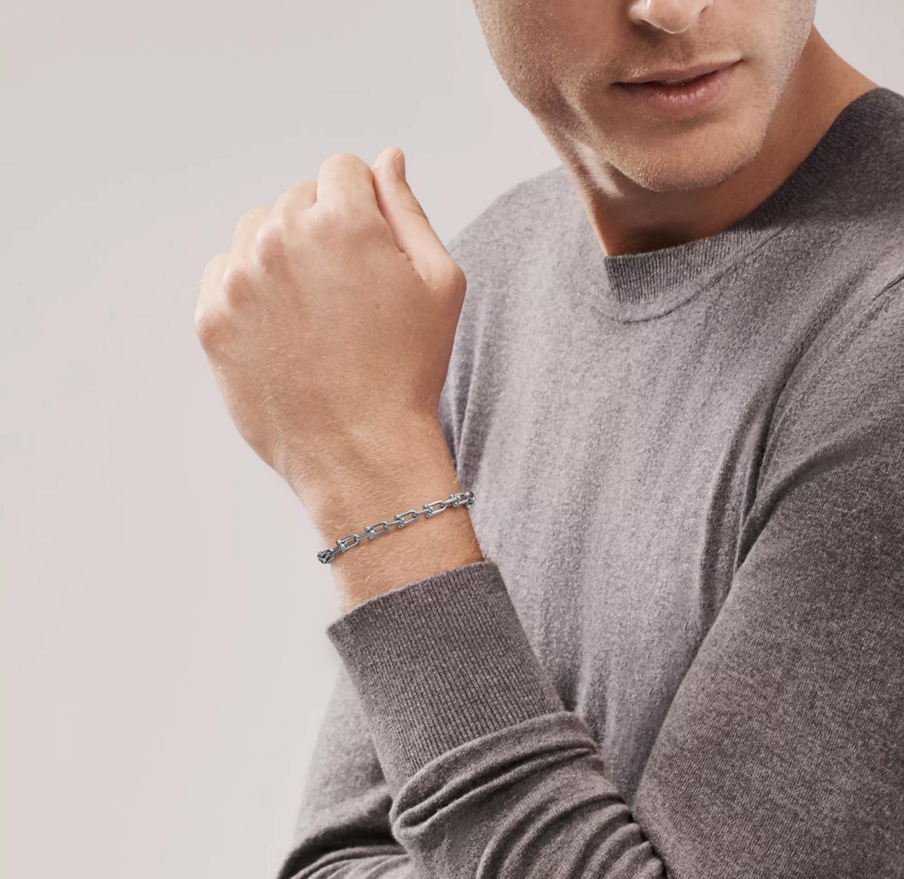 Man wearing a gray sweater and bracelet on a plain background