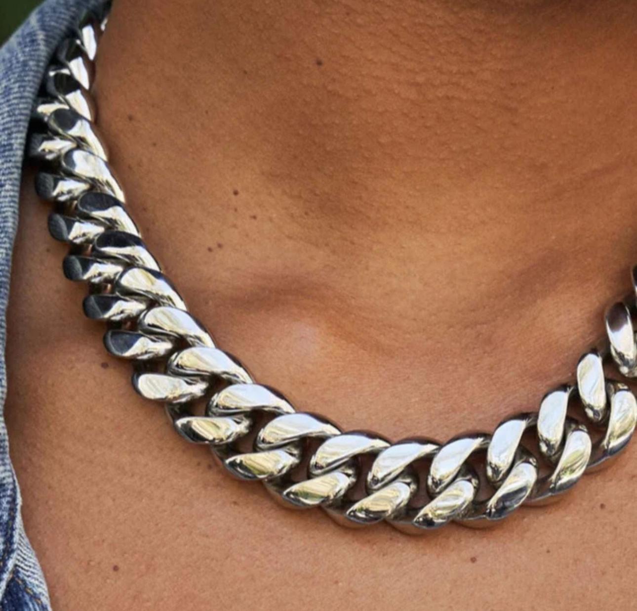 Close-up of a person wearing a silver cuban link necklace with a blurred background