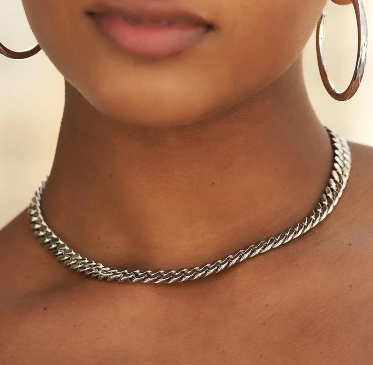 Close-up of a person wearing a silver cuban link necklace with a blurred background