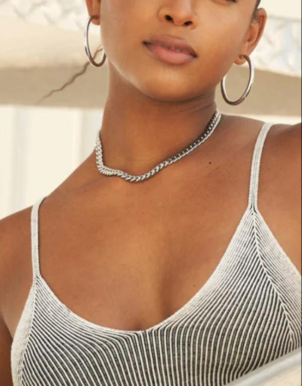 Woman wearing a cuban link necklace with thin straps, standing by a railing.