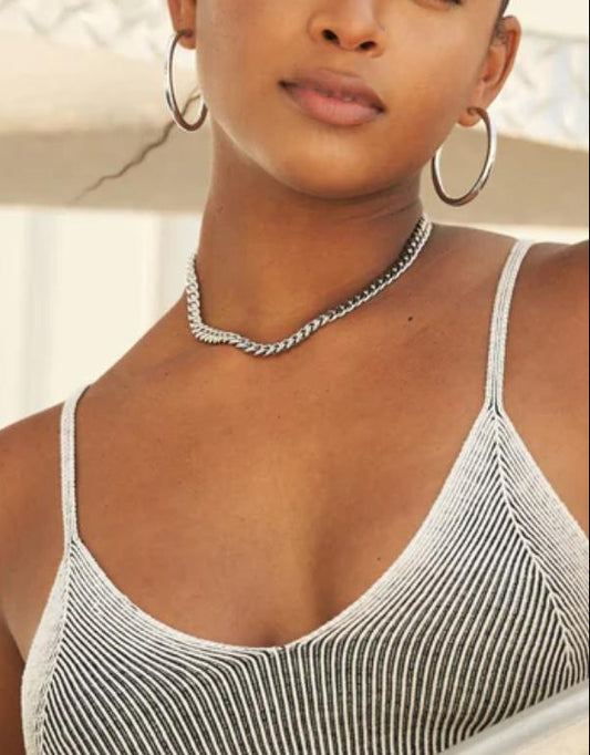 Woman wearing a cuban link necklace with thin straps, standing by a railing.
