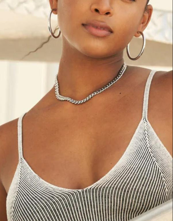 Woman wearing a cuban link necklace with thin straps, standing by a railing.