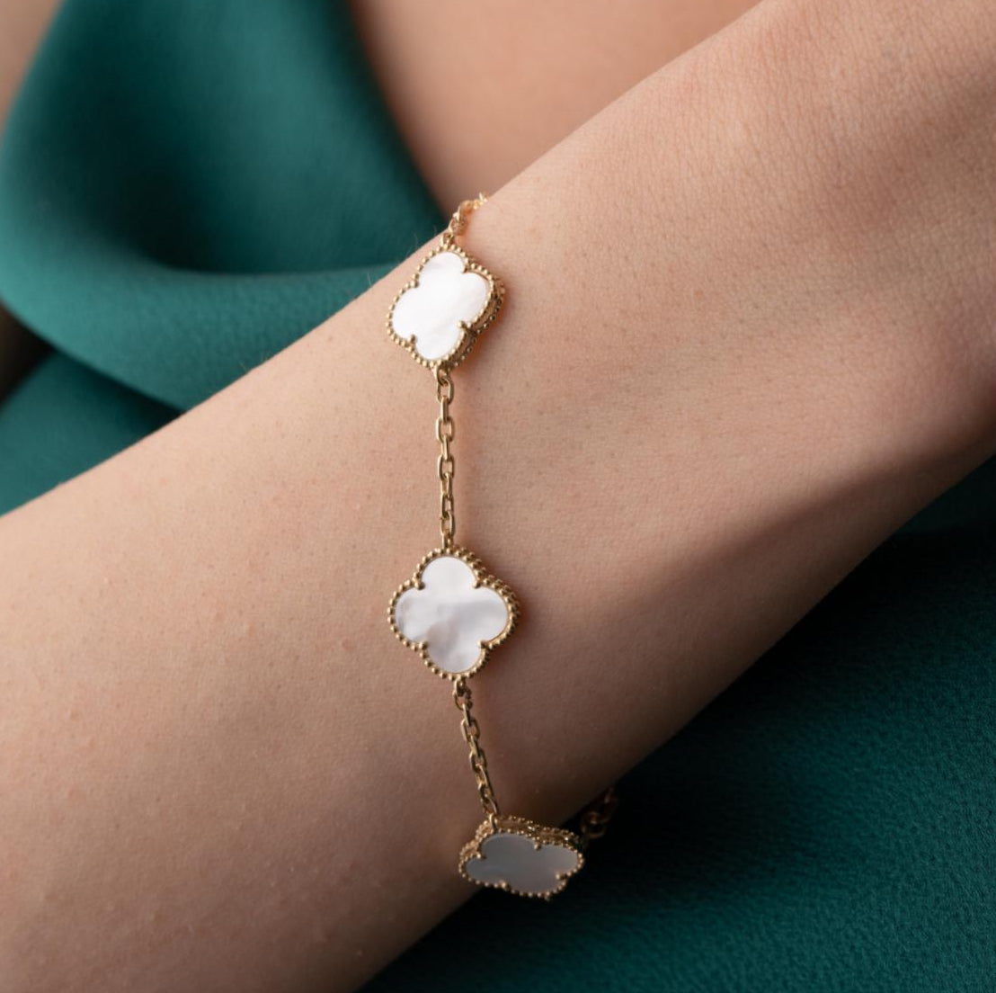 Gold bracelet with floral designs worn by a person on a white background