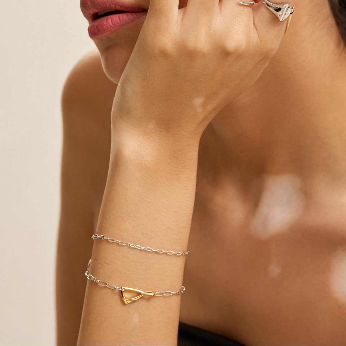 Woman wearing multiple gold and silver rings and bracelets on a neutral background