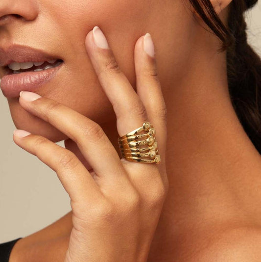 Close-up of a hand wearing multiple gold rings with a neutral background