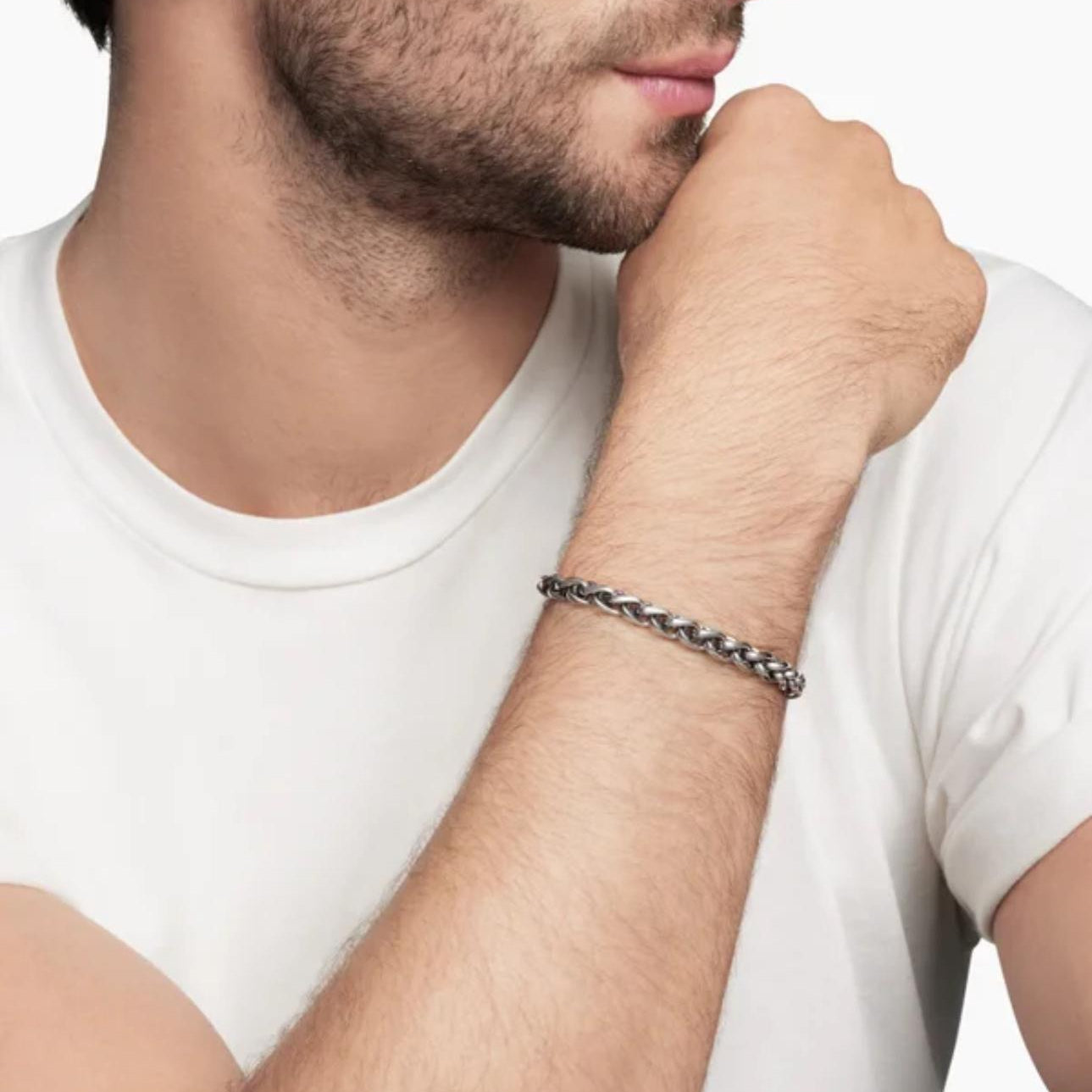 Man wearing a silver chain bracelet on his wrist, with a plain background