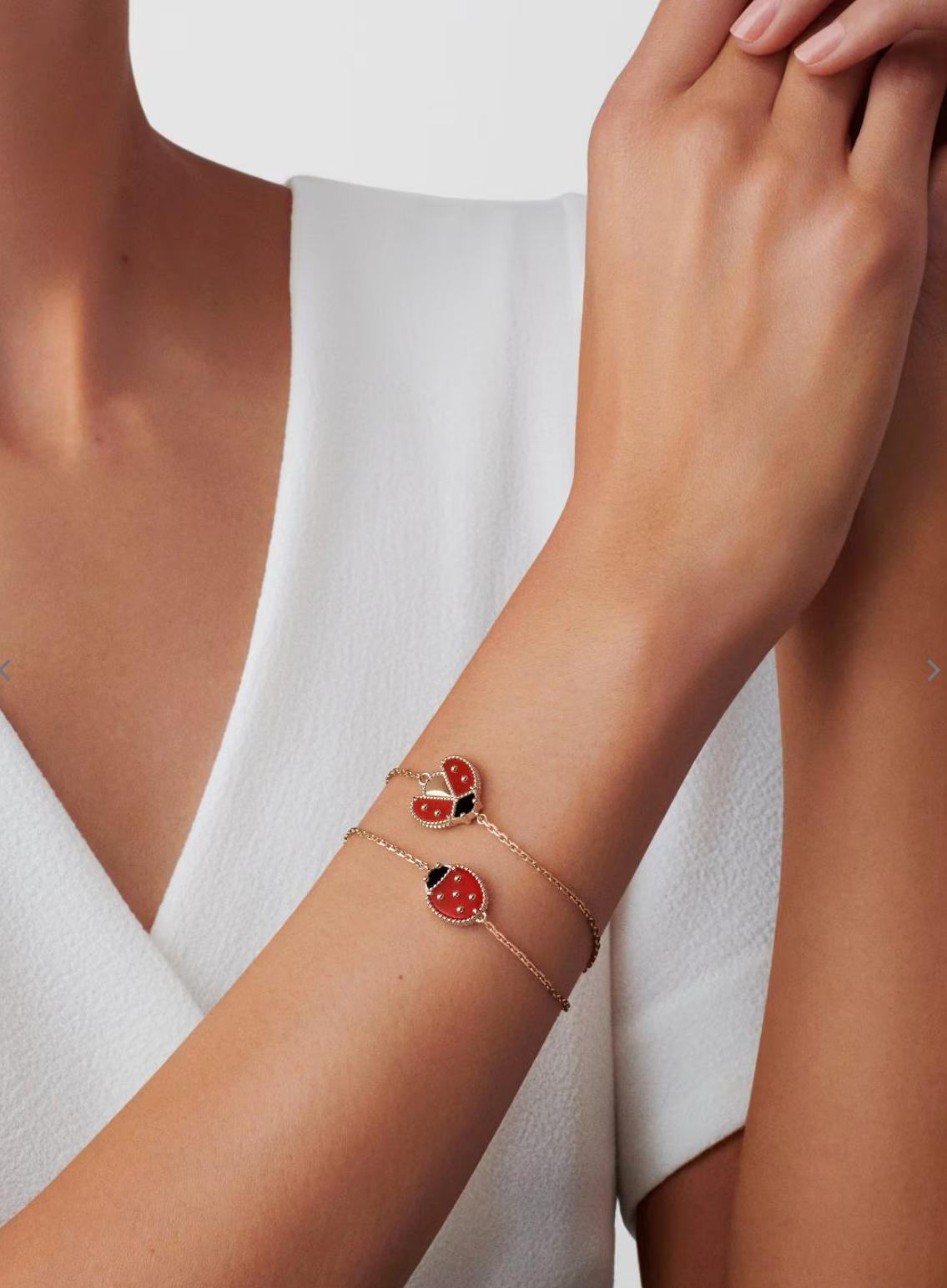 Close-up of a wrist wearing a delicate bracelet with ladybug charms against a white background
