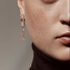 Close-up of a person wearing a rose gold chain earring with a neutral background