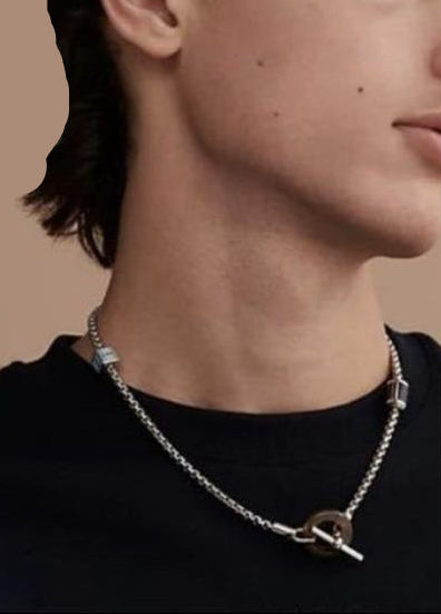 Close-up of a person wearing a silver necklace with a key pendant on a beige background