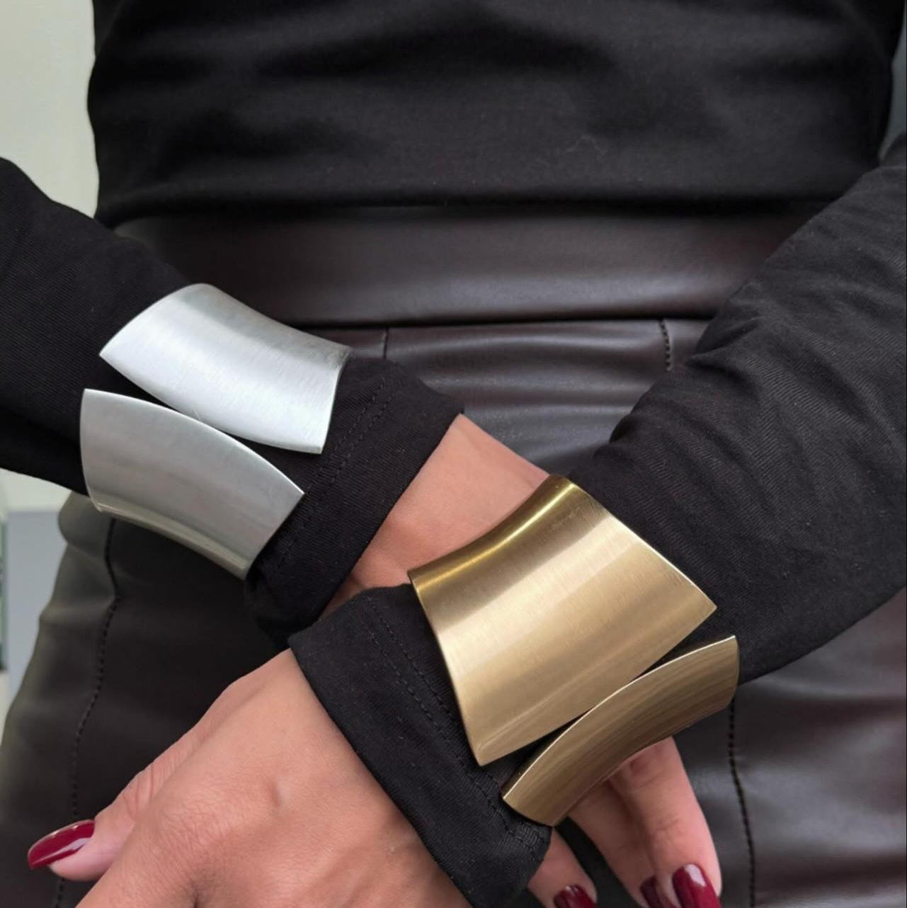 Close-up of hands wearing gold and silver cuff bracelets on a blurred background